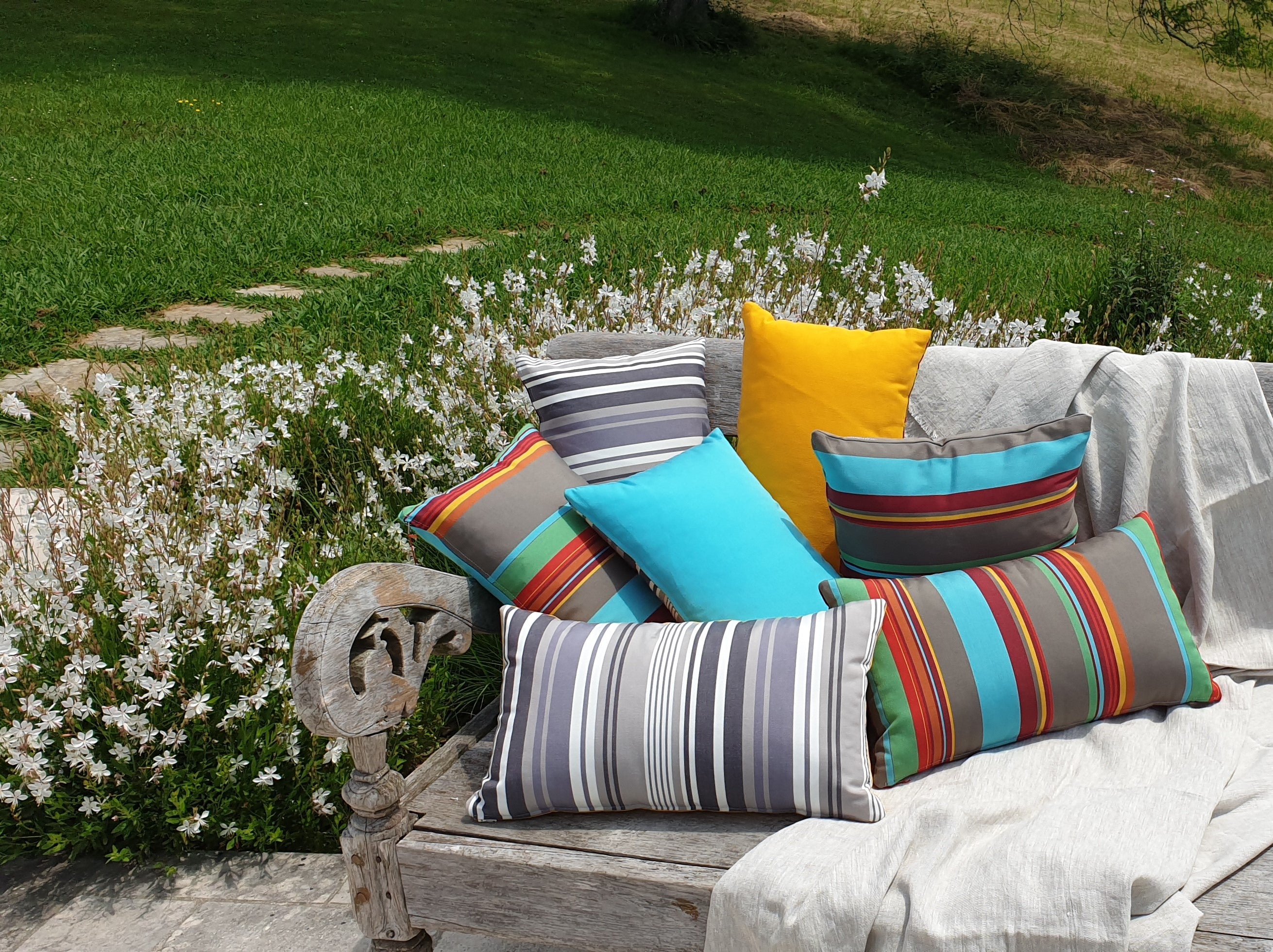 Coussins d'extérieur fabriqués en France par l'atelier Larouquine à Bayonne, posés sur le banc d'une terrasse.